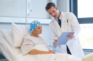 A doctor is seen discussing medical test results with a female patient in a hospital ward. The doctor is showing the patient her medical records and explaining the potential side effects of the treatment intervention.