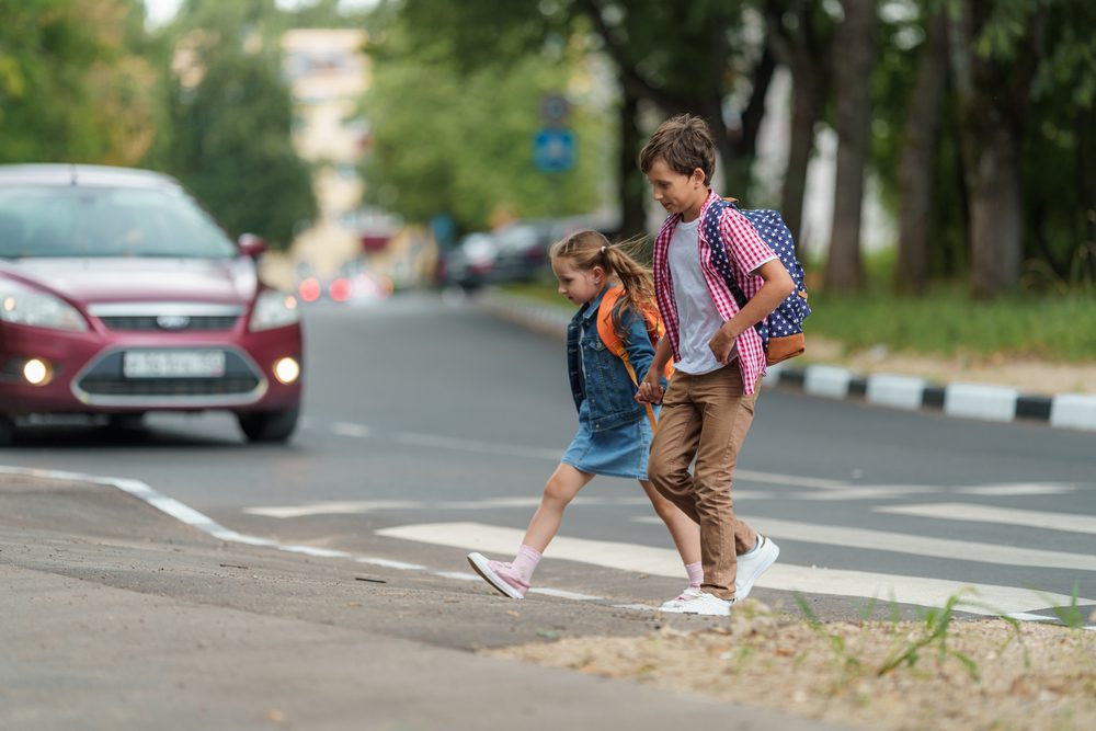 Two young children holding hands while crossing the street, vulnerable to an Alabama pedestrian accident.