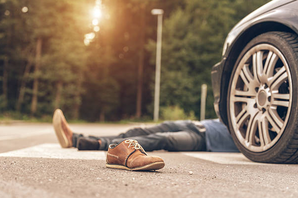 Injured pedestrian lies in the road near a car, a shoe knocked loose, after a hit-and-run accident in Birmingham