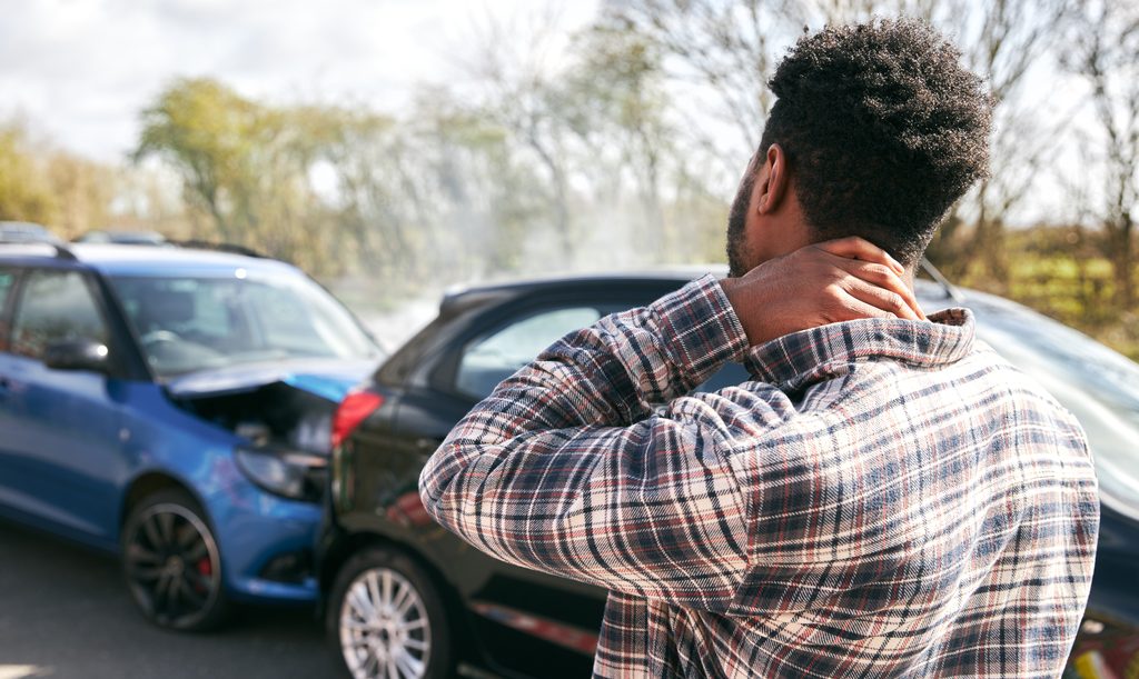 Man holding the back of his neck after a rear-end collision between a blue car and a dark hatchback